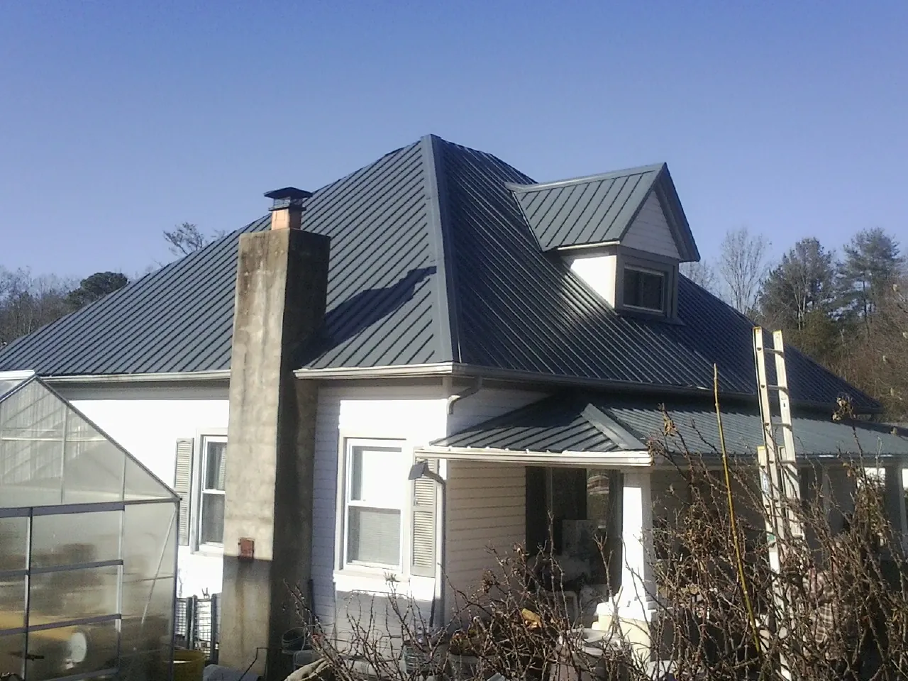 Dark blue standing seam metal roof on a white farmhouse with dormer — Slate & Tile Roof Repair by Roofing Brothers in Melissa