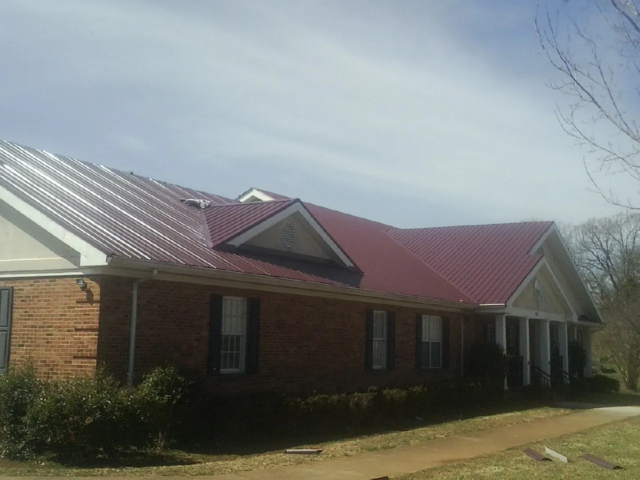 Red metal roof with gabled entries on a long brick building, from a Hail Damage Roof Repair job in Melissa