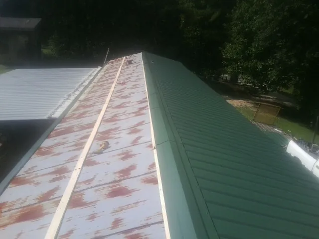 Old rusted panels beside newly installed green metal roofing — Wind Damage Roof Repair by Roofing Brothers in Melissa