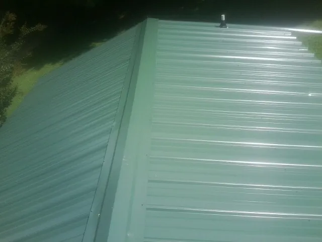 New green metal panels meeting at the ridge of a roof — Flat Roof Repair work by our crew in Melissa