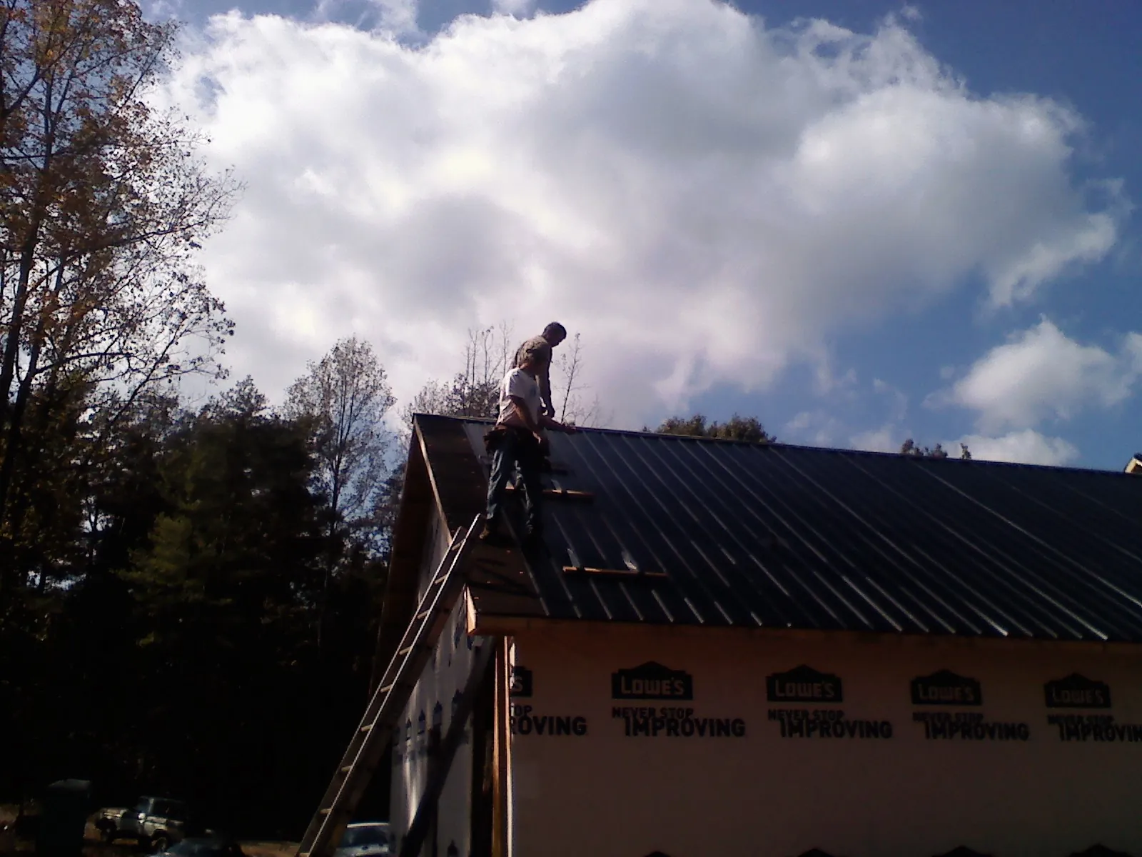Roofer fastening dark metal panels high against a cloudy sky, from a Roof Inspection job in Melissa