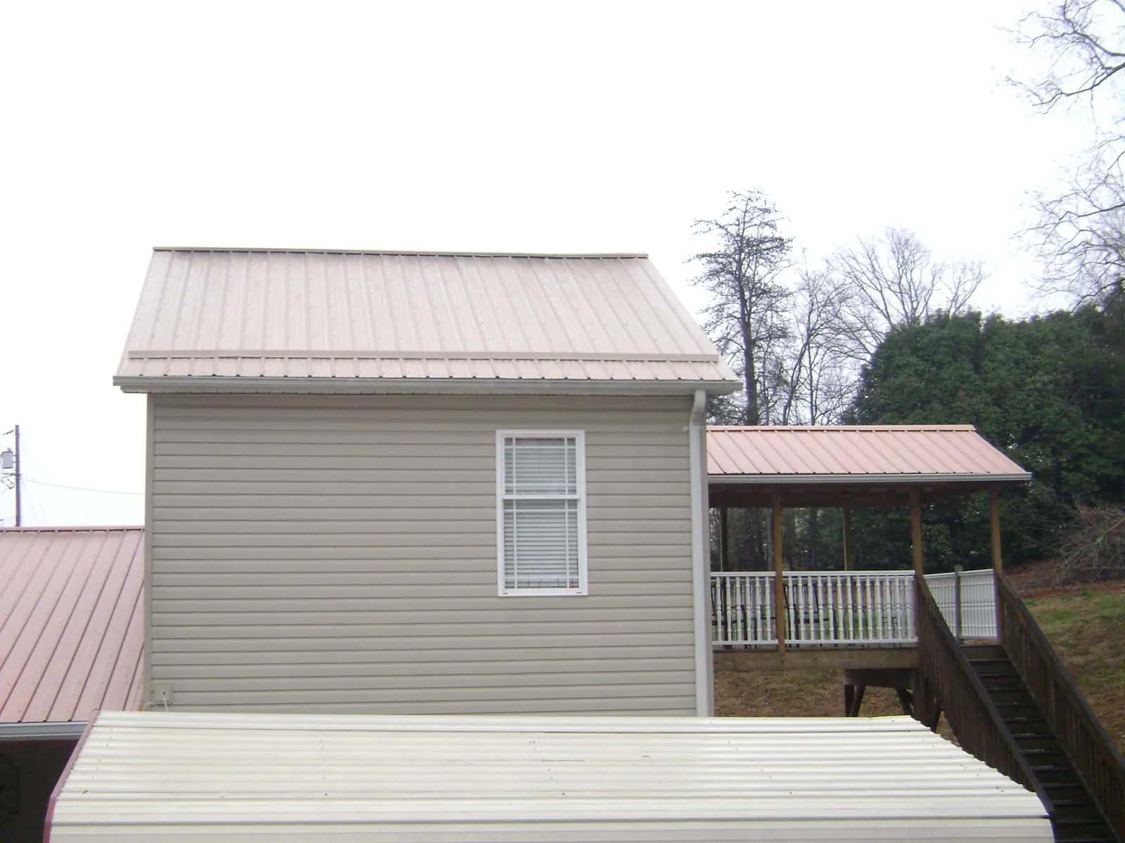 Tan metal roofs on a two story addition and attached porch, from a Roof Replacement job in Melissa